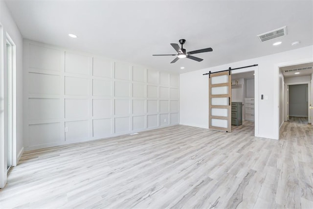 unfurnished living room with light wood-type flooring, a barn door, and ceiling fan