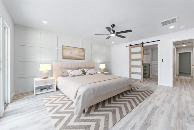 bedroom with ceiling fan, a barn door, and light hardwood / wood-style floors