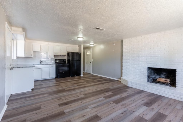 kitchen with sink, a brick fireplace, black fridge, stove, and white cabinets