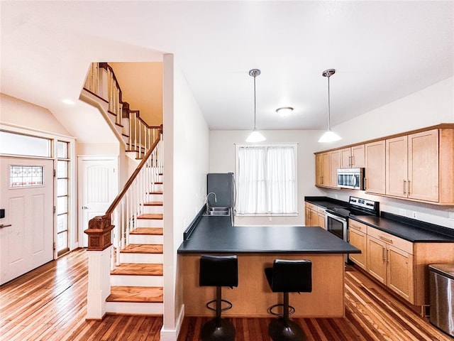 kitchen featuring light brown cabinetry, stainless steel appliances, hanging light fixtures, and dark wood-type flooring