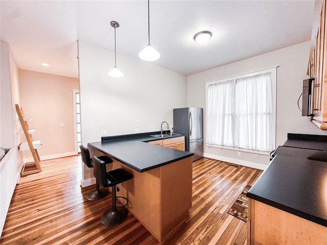 kitchen with kitchen peninsula, a kitchen bar, light hardwood / wood-style flooring, stainless steel refrigerator, and hanging light fixtures