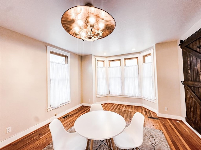 dining space with hardwood / wood-style floors, a notable chandelier, and a barn door