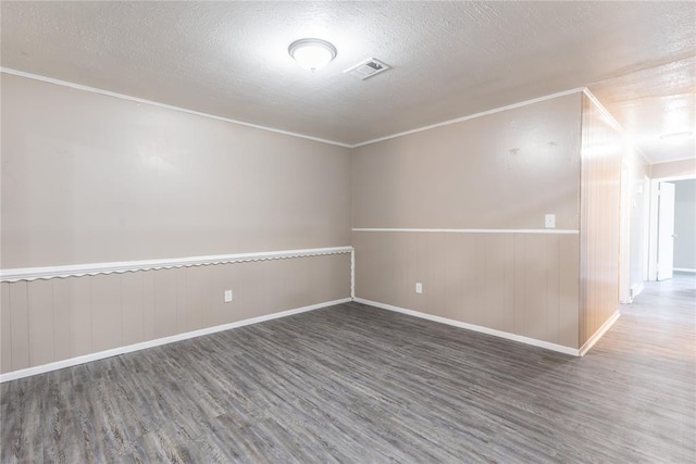 spare room with crown molding, wood walls, dark wood-type flooring, and a textured ceiling