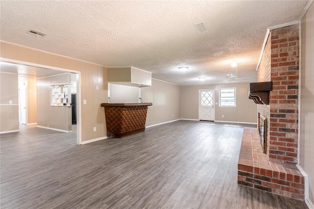 unfurnished living room featuring a textured ceiling, ornamental molding, dark wood-type flooring, and a brick fireplace