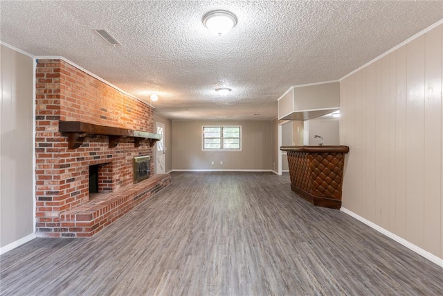 unfurnished living room featuring a brick fireplace, ornamental molding, a textured ceiling, wooden walls, and hardwood / wood-style floors