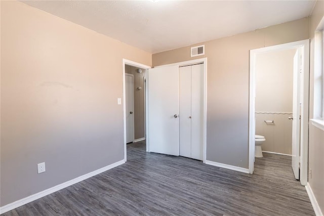 unfurnished bedroom with dark hardwood / wood-style flooring, ensuite bathroom, and a closet