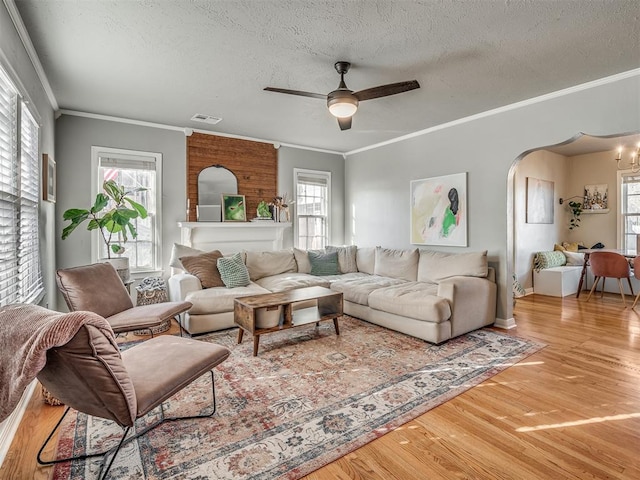 living room with ceiling fan with notable chandelier, wood-type flooring, a textured ceiling, and ornamental molding