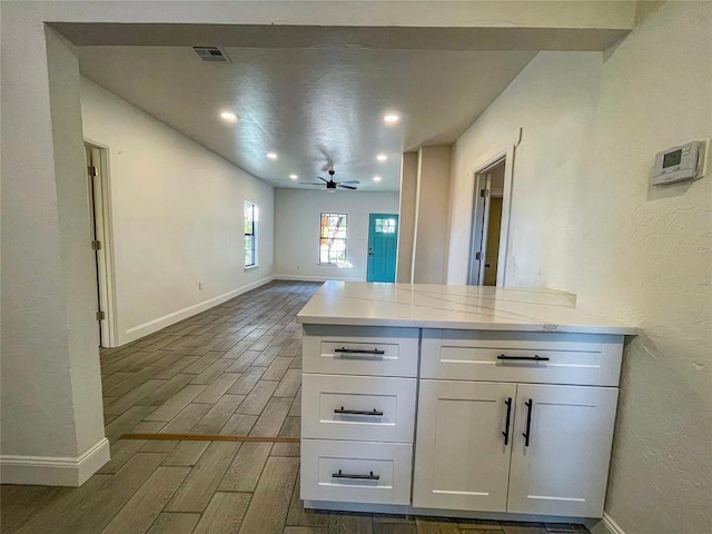 kitchen featuring white cabinets, kitchen peninsula, light stone counters, and ceiling fan