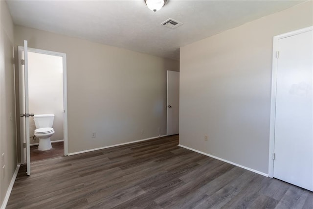 unfurnished bedroom featuring ensuite bath and dark hardwood / wood-style floors