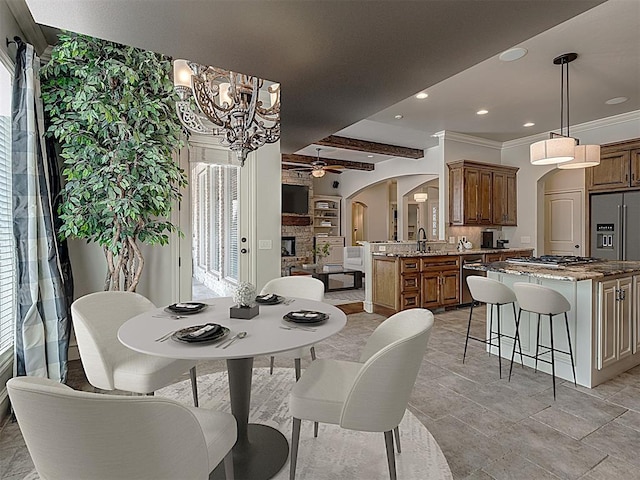 dining room featuring crown molding, a fireplace, beamed ceiling, and ceiling fan with notable chandelier