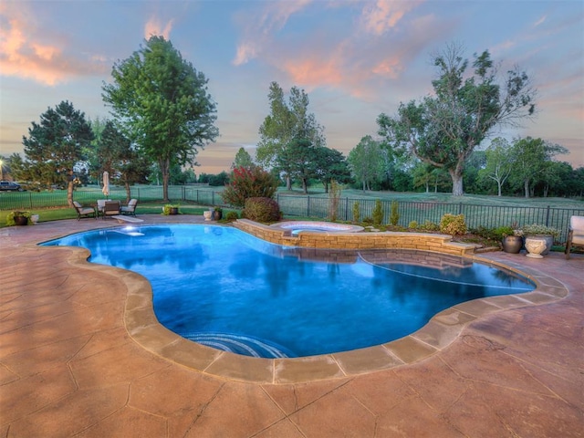 pool at dusk with an in ground hot tub and a patio