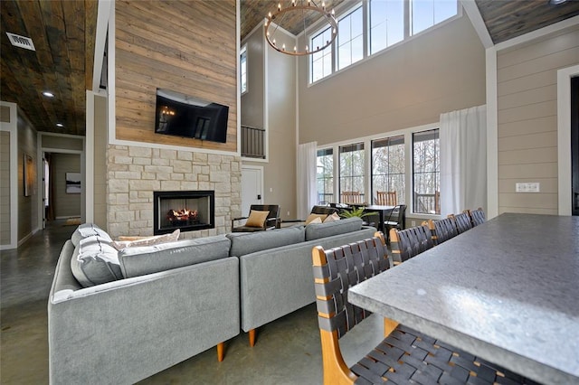 living room with finished concrete flooring, a stone fireplace, wood walls, and a chandelier