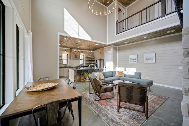 living room featuring a notable chandelier, visible vents, a towering ceiling, wood walls, and concrete floors