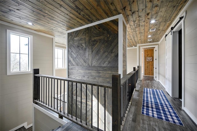 hallway with a barn door, wood ceiling, wood finished floors, an upstairs landing, and recessed lighting