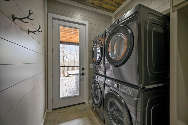 clothes washing area featuring laundry area, wooden walls, and stacked washer / drying machine