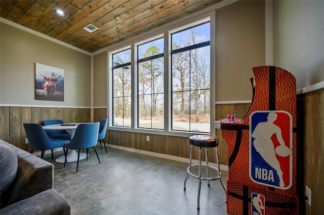 living area with wooden walls, a wainscoted wall, visible vents, wood ceiling, and finished concrete flooring