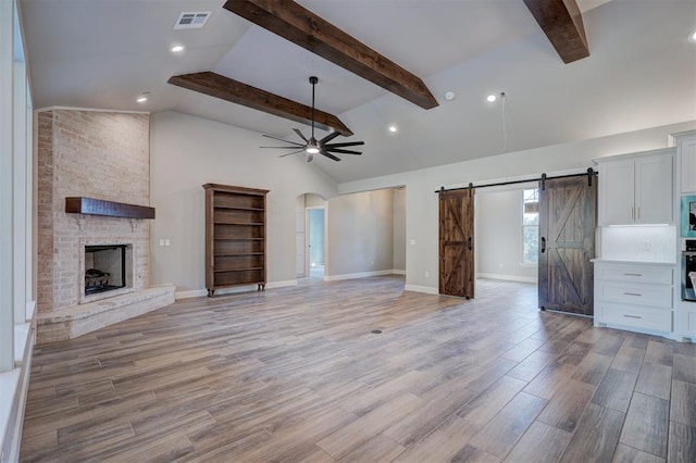 unfurnished living room featuring a barn door, ceiling fan, a fireplace, and lofted ceiling with beams