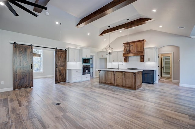 kitchen featuring a barn door, white cabinetry, oven, hanging light fixtures, and an island with sink