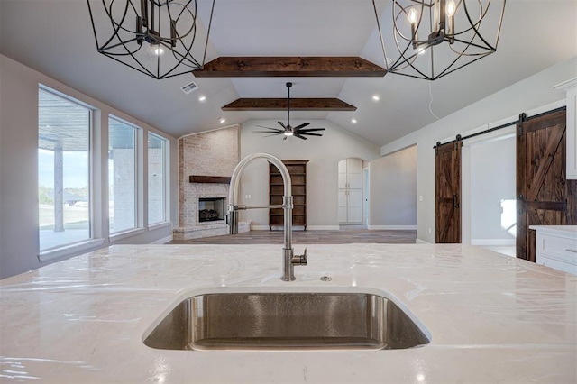 kitchen featuring sink, a barn door, light stone counters, vaulted ceiling with beams, and decorative light fixtures