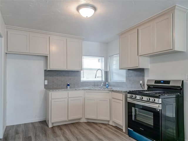 kitchen with light stone countertops, decorative backsplash, stainless steel gas range oven, sink, and light hardwood / wood-style floors