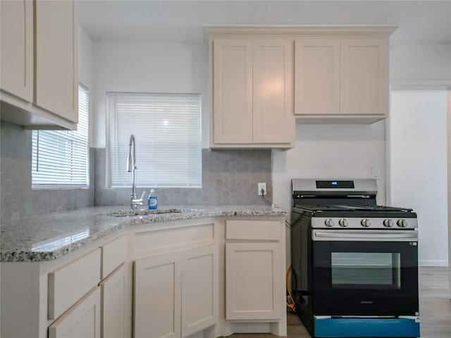 kitchen featuring backsplash, sink, light stone countertops, white cabinetry, and range with gas cooktop