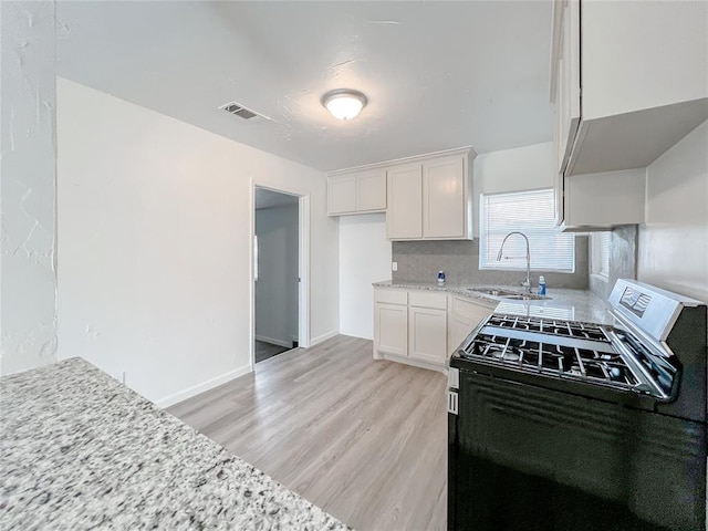 kitchen featuring sink, black electric range, light hardwood / wood-style floors, light stone counters, and white cabinetry