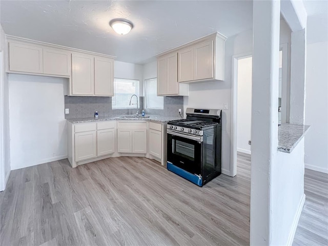 kitchen featuring light stone countertops, sink, stainless steel gas range, decorative backsplash, and white cabinets