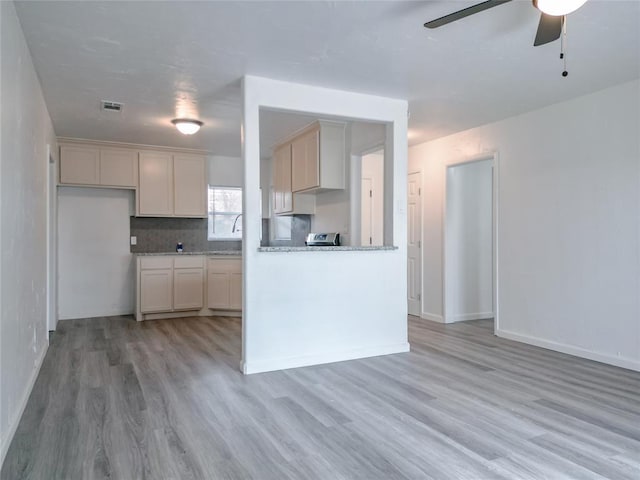 kitchen with backsplash, light stone counters, ceiling fan, range, and light hardwood / wood-style floors