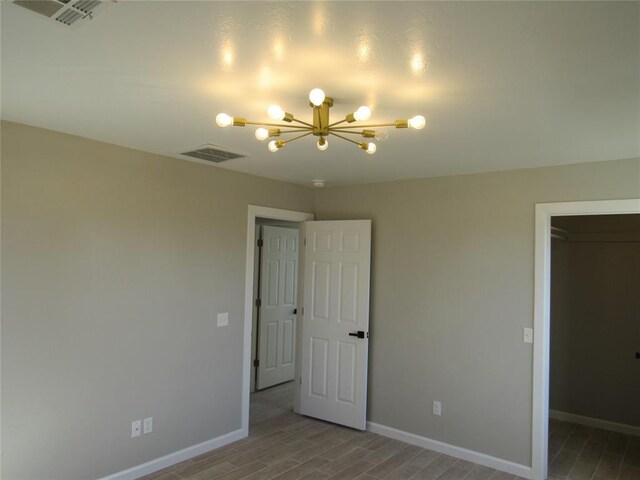 unfurnished bedroom with hardwood / wood-style floors, a closet, a walk in closet, and a chandelier