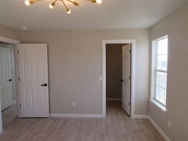 unfurnished bedroom featuring a walk in closet, a closet, multiple windows, and an inviting chandelier