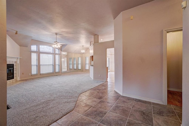 unfurnished living room with vaulted ceiling, a tile fireplace, ceiling fan with notable chandelier, and dark colored carpet