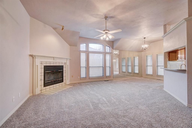 unfurnished living room with a tile fireplace, lofted ceiling, light colored carpet, and ceiling fan with notable chandelier