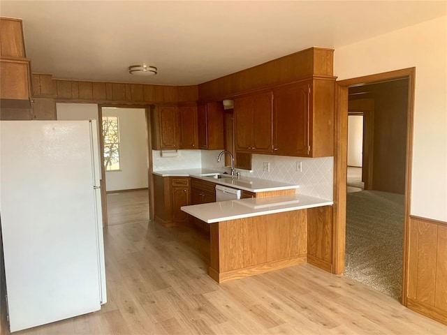 kitchen featuring sink, kitchen peninsula, light hardwood / wood-style floors, white appliances, and decorative backsplash