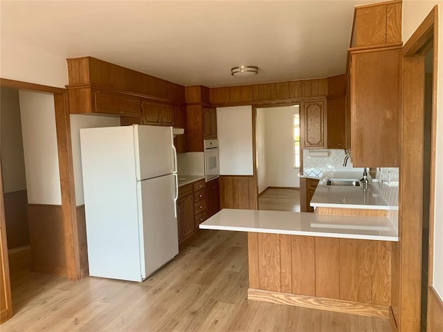 kitchen featuring wood walls, white appliances, sink, light hardwood / wood-style flooring, and kitchen peninsula