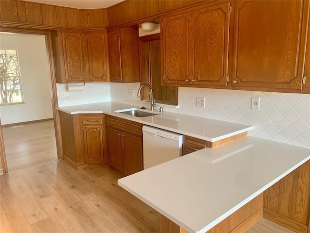 kitchen featuring white dishwasher, sink, decorative backsplash, light hardwood / wood-style floors, and kitchen peninsula