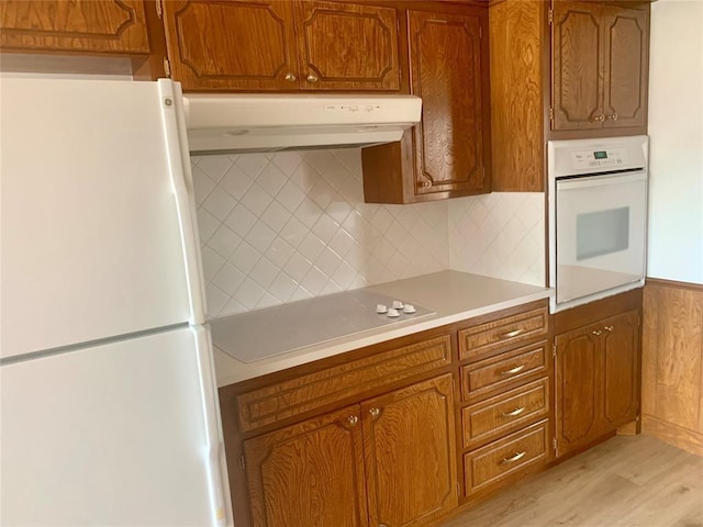 kitchen with tasteful backsplash, white appliances, and light wood-type flooring