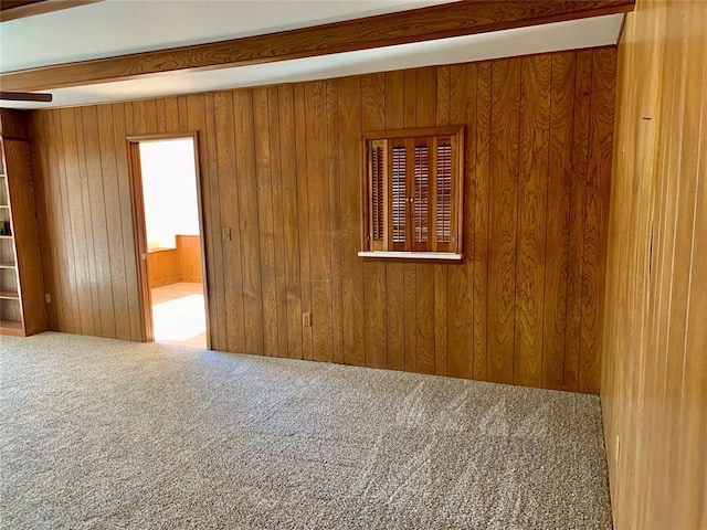 carpeted empty room with beamed ceiling and wooden walls