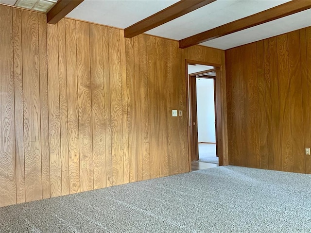 empty room featuring beamed ceiling, wood walls, and carpet