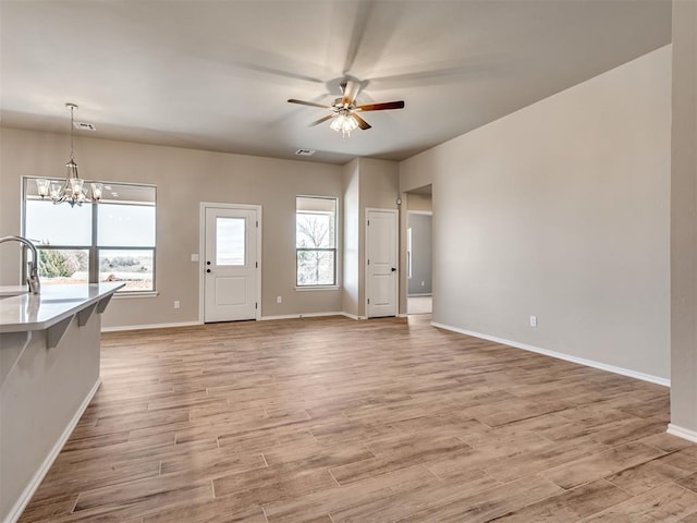 unfurnished living room featuring light wood-type flooring, a sink, baseboards, and ceiling fan with notable chandelier