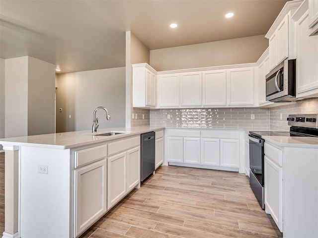 kitchen featuring a peninsula, a sink, white cabinets, light countertops, and appliances with stainless steel finishes