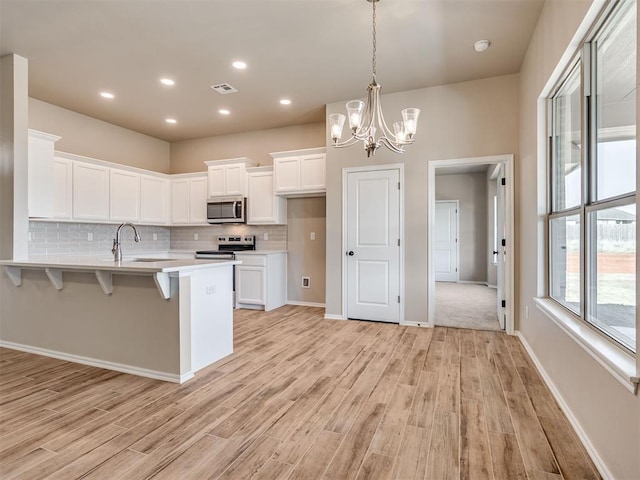 kitchen with white cabinets, a kitchen bar, stainless steel appliances, and light countertops