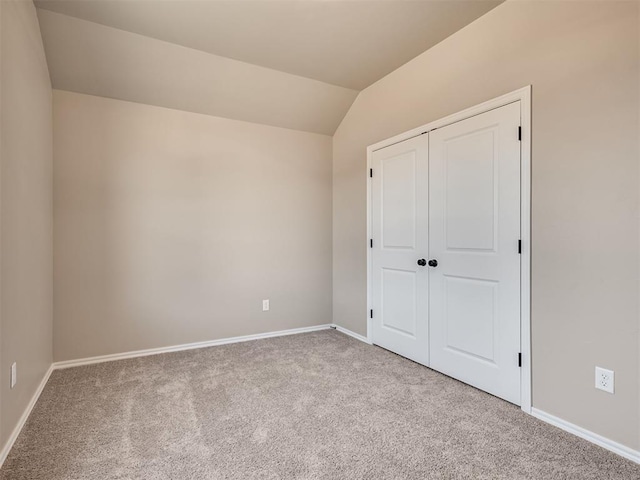 unfurnished bedroom with baseboards, a closet, lofted ceiling, and light colored carpet