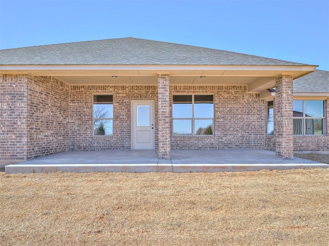 property entrance with a patio, brick siding, and a shingled roof