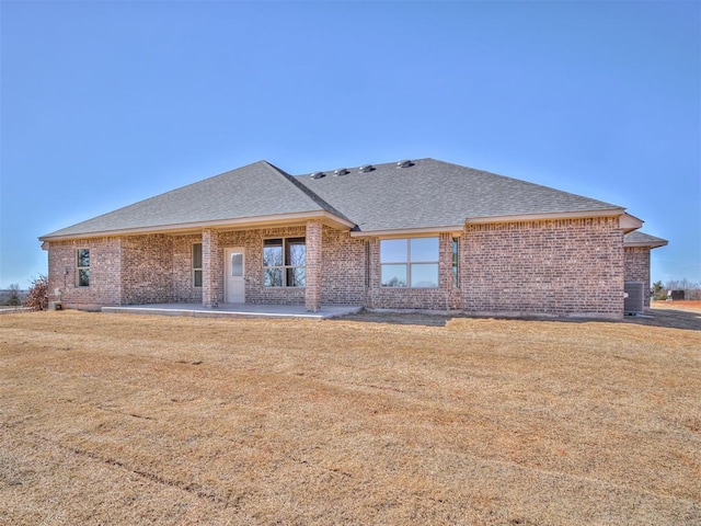 back of house featuring brick siding, a patio, a shingled roof, a lawn, and central AC unit