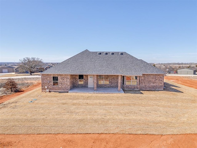 rear view of property with a patio area, brick siding, a lawn, and roof with shingles