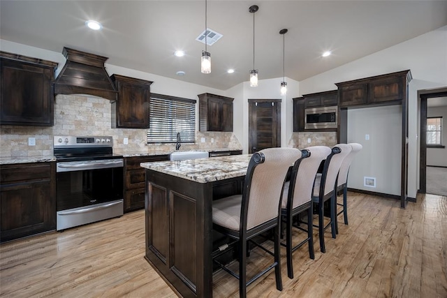 kitchen with light stone countertops, backsplash, vaulted ceiling, appliances with stainless steel finishes, and custom exhaust hood