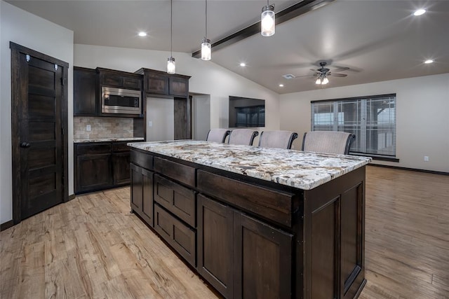 kitchen featuring tasteful backsplash, stainless steel microwave, ceiling fan, a kitchen island, and hanging light fixtures