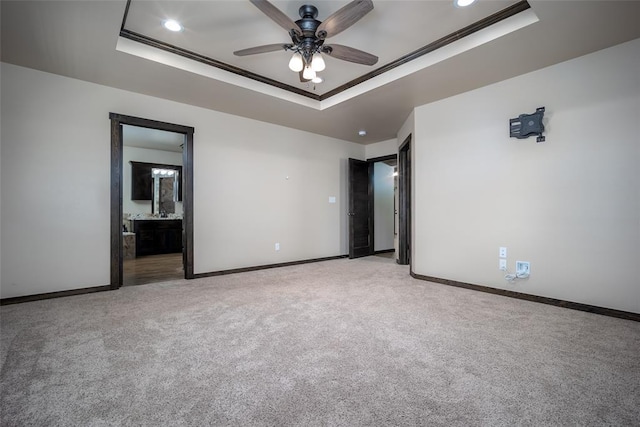 unfurnished bedroom featuring ensuite bath, ceiling fan, crown molding, light colored carpet, and a tray ceiling