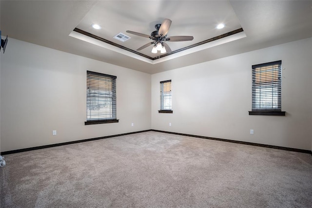 carpeted empty room with a raised ceiling, ceiling fan, and ornamental molding