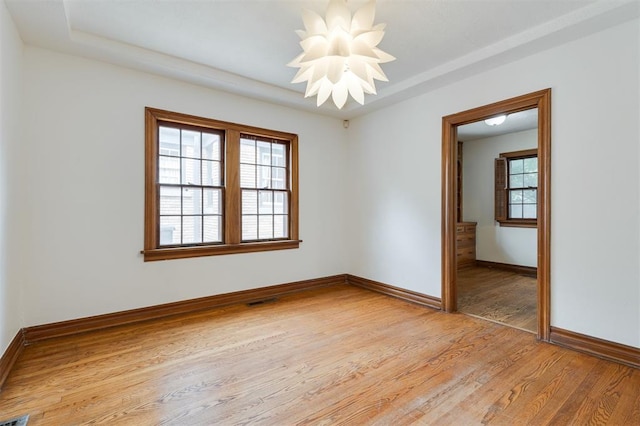 spare room featuring a tray ceiling, a notable chandelier, and light wood-type flooring